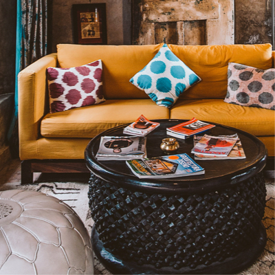 A living room featuring a mustard mid-century couch and round black coffee table topped with magazines.